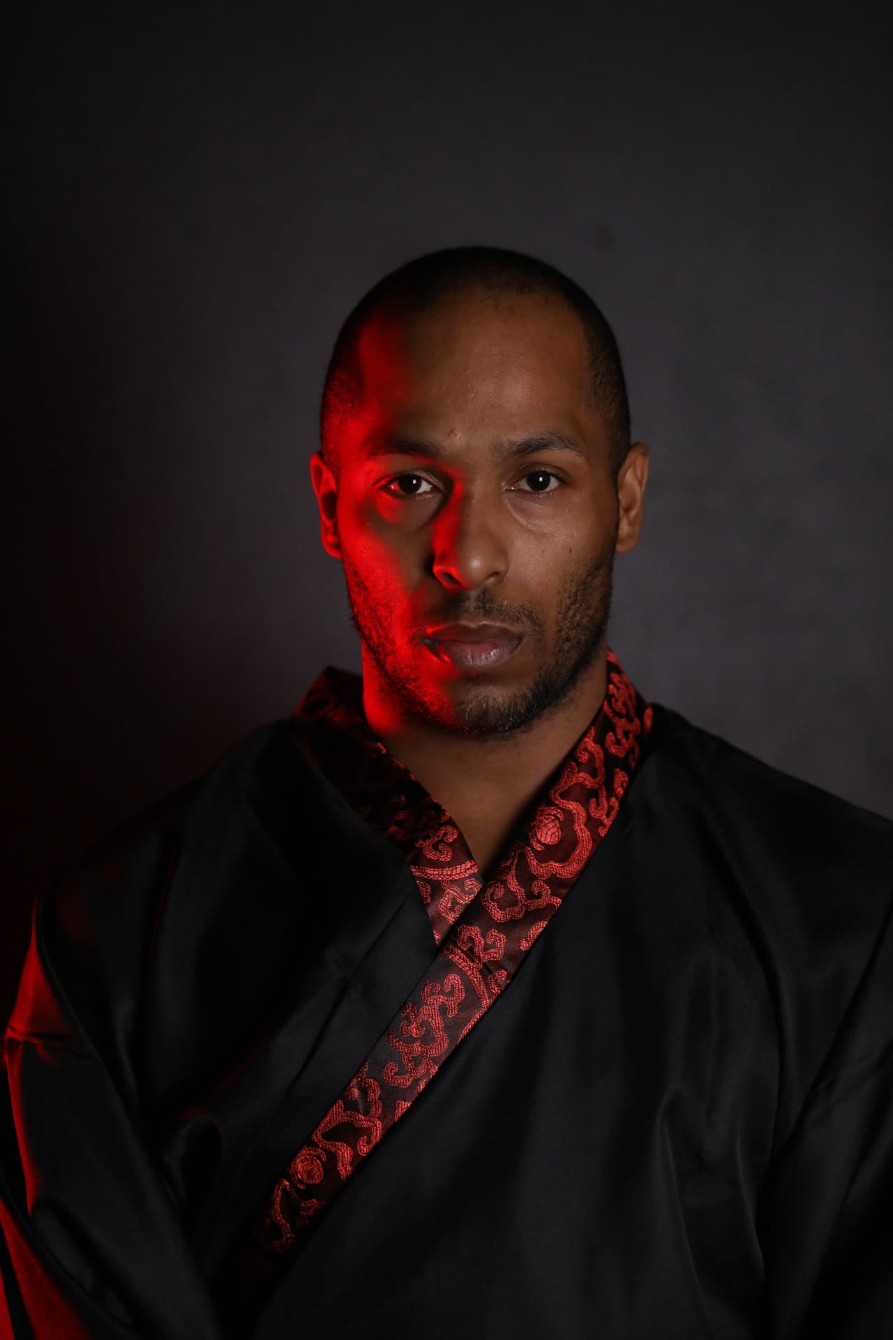 Portrait of Sir Pocketz in a black robe with red brocade trim, lit from the side with red light